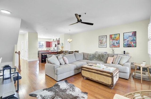 living area with baseboards, light wood finished floors, and ceiling fan with notable chandelier