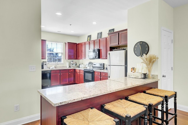 kitchen featuring a sink, black appliances, dark brown cabinets, wood finished floors, and baseboards