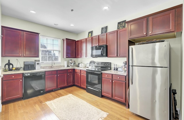 kitchen with recessed lighting, a sink, dark brown cabinets, light wood-type flooring, and black appliances