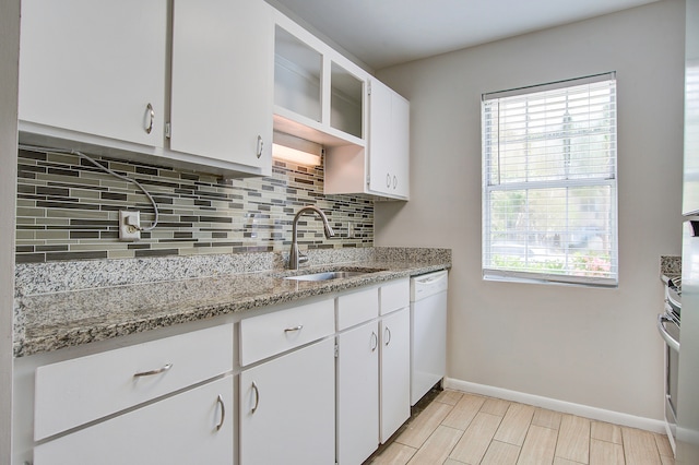 kitchen featuring light stone counters, white cabinets, white dishwasher, sink, and backsplash