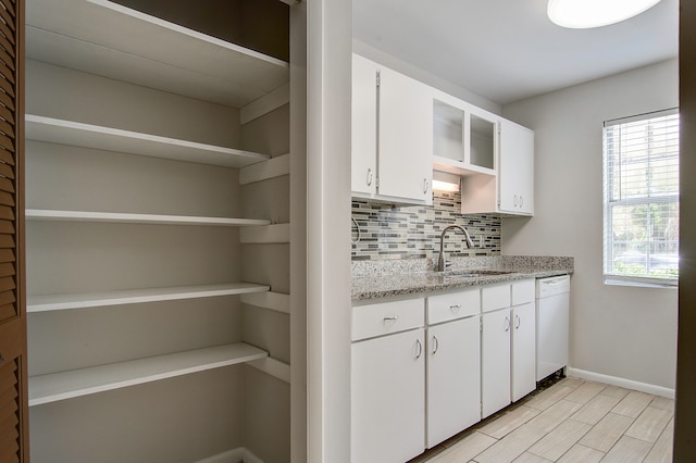 kitchen with light stone countertops, decorative backsplash, white cabinets, sink, and dishwasher