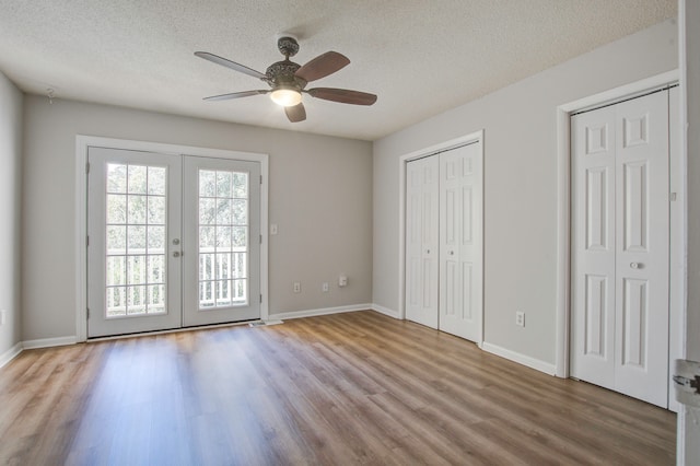 unfurnished bedroom with ceiling fan, french doors, a textured ceiling, multiple closets, and light hardwood / wood-style floors