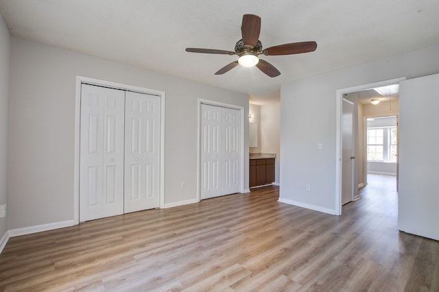 unfurnished bedroom with ceiling fan, a textured ceiling, two closets, light wood-type flooring, and ensuite bath