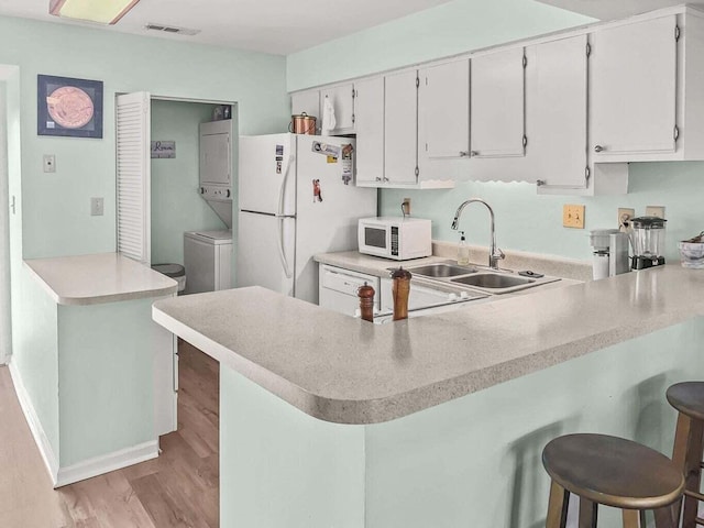 kitchen featuring white appliances, visible vents, light wood-style flooring, a peninsula, and a sink