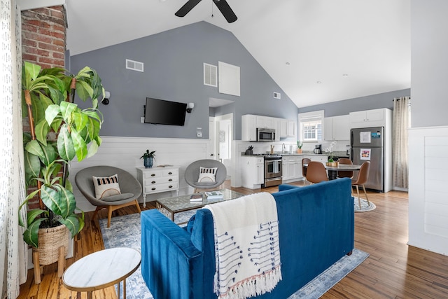 170 Spring St, Charleston, SC 29403 - living room featuring a ceiling fan, wainscoting, high vaulted ceiling, and light wood-type flooring