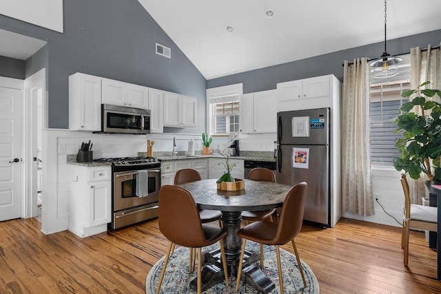 170 Spring St, Charleston, SC 29403 - kitchen featuring appliances with stainless steel finishes, high vaulted ceiling, light wood-type flooring, white cabinets, and hanging light fixtures