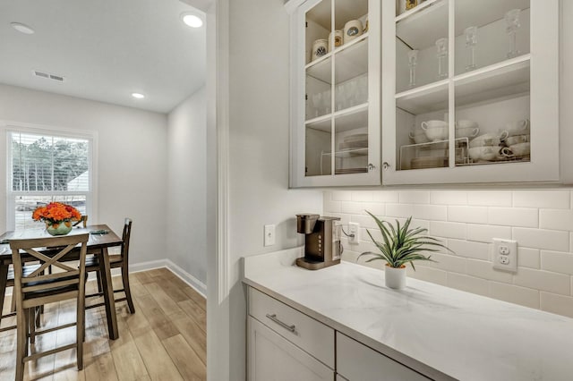 bar featuring tasteful backsplash, light stone counters, white cabinets, and light wood-type flooring