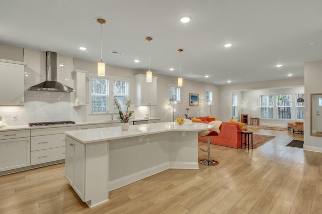 kitchen featuring a kitchen island, decorative light fixtures, white cabinets, and wall chimney exhaust hood