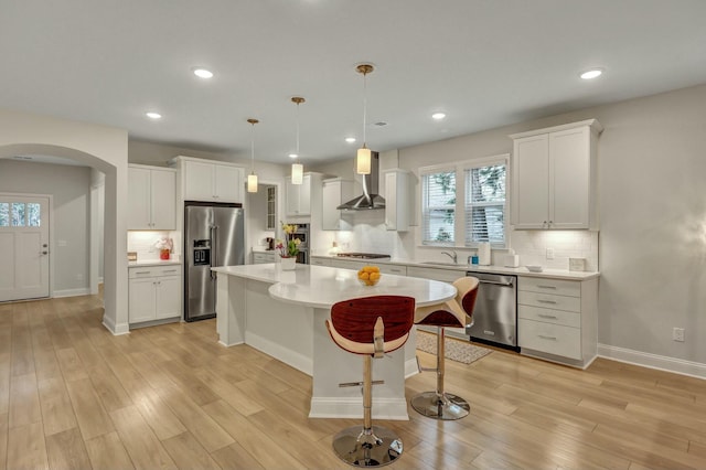 kitchen with white cabinetry, hanging light fixtures, a center island, stainless steel appliances, and wall chimney range hood