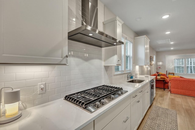 kitchen featuring sink, wall chimney exhaust hood, white cabinets, decorative backsplash, and stainless steel gas stovetop