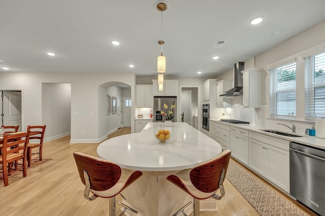 kitchen with sink, hanging light fixtures, stainless steel appliances, a kitchen island, and wall chimney exhaust hood