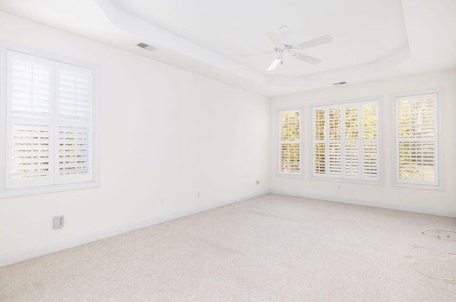 carpeted spare room featuring ceiling fan, a healthy amount of sunlight, and a raised ceiling