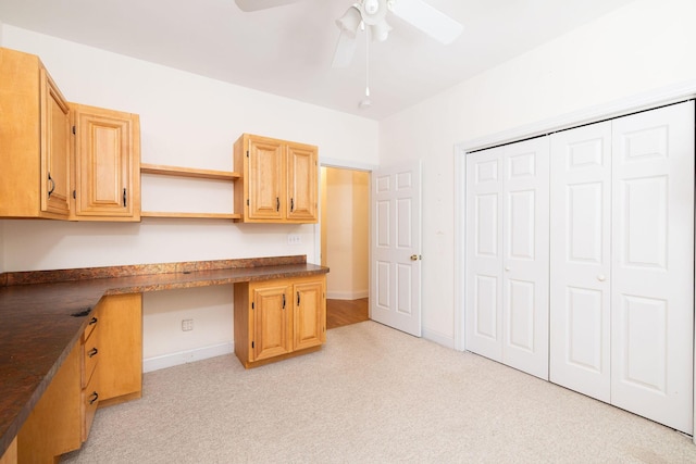 unfurnished office with ceiling fan, light colored carpet, and built in desk