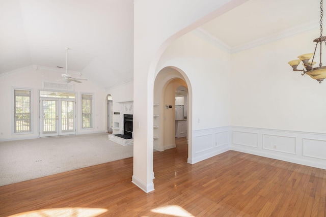 unfurnished living room featuring built in shelves, a high end fireplace, lofted ceiling, carpet, and ceiling fan with notable chandelier