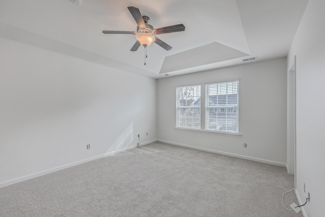 empty room with a tray ceiling, light carpet, and ceiling fan