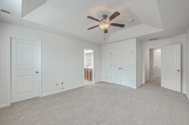 unfurnished bedroom with a raised ceiling, light carpet, and ceiling fan