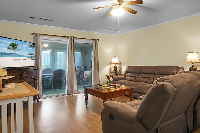 living area with ornamental molding, visible vents, ceiling fan, and wood finished floors