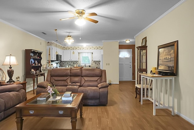 living room featuring light wood finished floors, baseboards, ornamental molding, and a ceiling fan