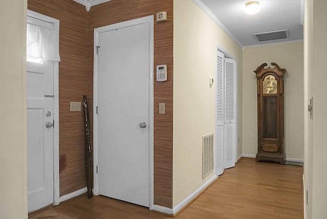 corridor featuring ornamental molding, visible vents, light wood-style floors, and baseboards