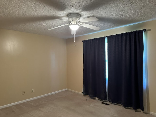empty room featuring ceiling fan, a textured ceiling, visible vents, baseboards, and light carpet