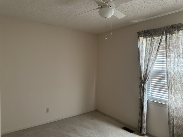 spare room featuring visible vents, baseboards, ceiling fan, light colored carpet, and a textured ceiling