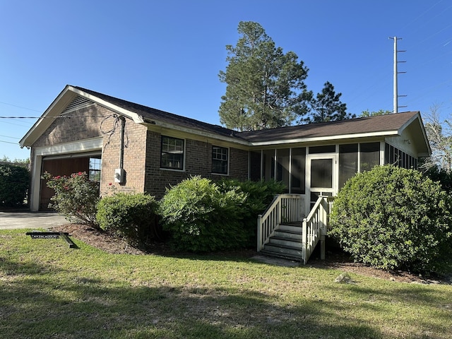 single story home with a sunroom, a garage, a front lawn, and brick siding