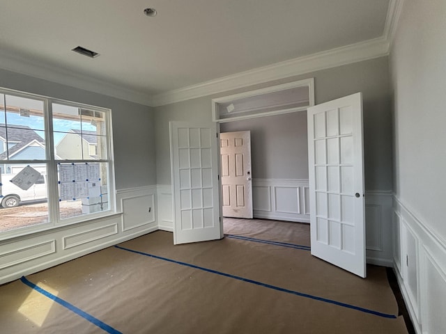 unfurnished bedroom featuring a wainscoted wall, a decorative wall, visible vents, and crown molding