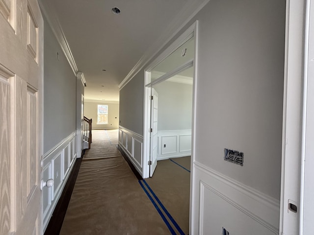 hallway with a wainscoted wall, ornamental molding, a decorative wall, and dark colored carpet