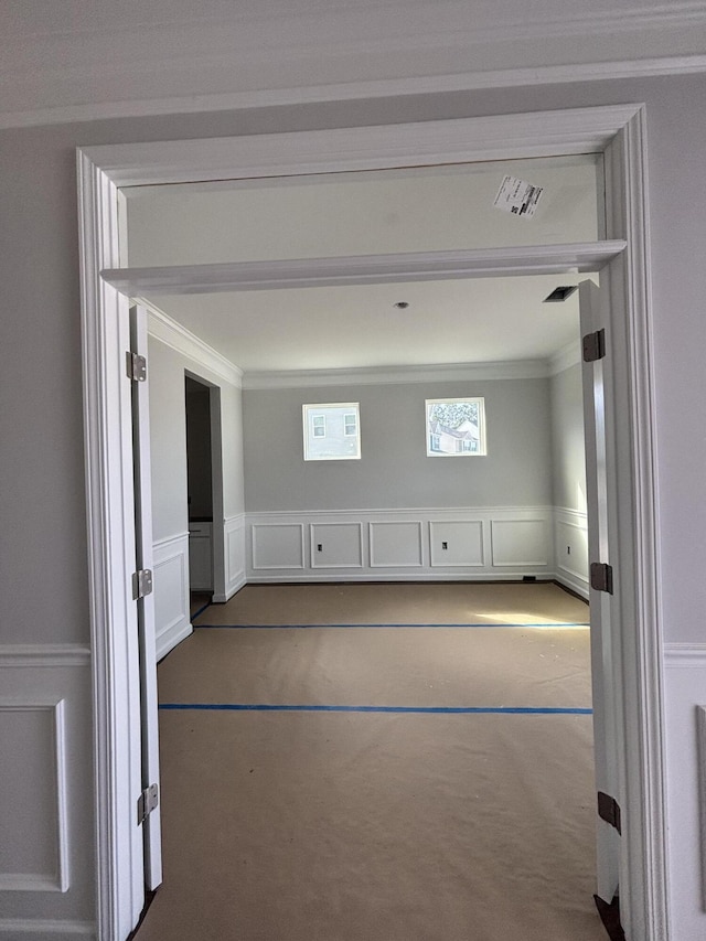 spare room featuring ornamental molding, a decorative wall, and wainscoting