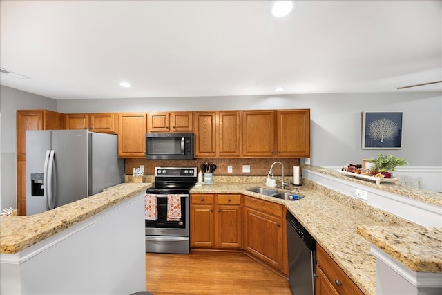 kitchen with light stone counters, light wood-style flooring, appliances with stainless steel finishes, brown cabinets, and a sink