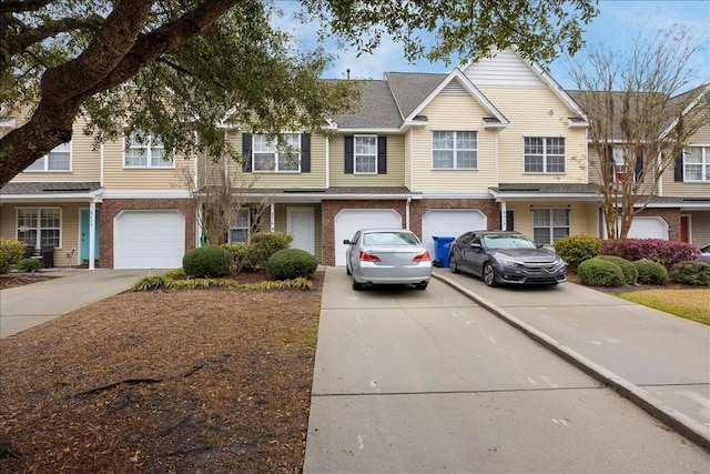 townhome / multi-family property featuring an attached garage, brick siding, driveway, and roof with shingles