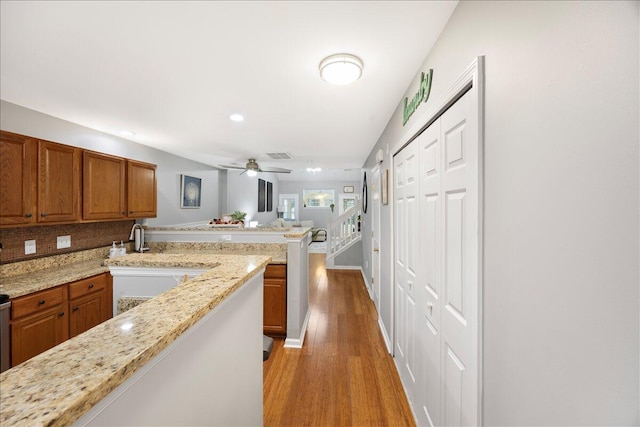 kitchen with a peninsula, brown cabinetry, visible vents, and light wood-type flooring