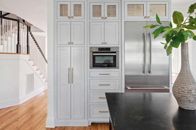 kitchen with baseboards, visible vents, stainless steel appliances, glass insert cabinets, and light wood-style floors