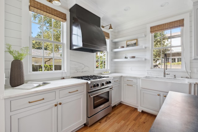 kitchen with stainless steel range, open shelves, backsplash, exhaust hood, and light wood finished floors