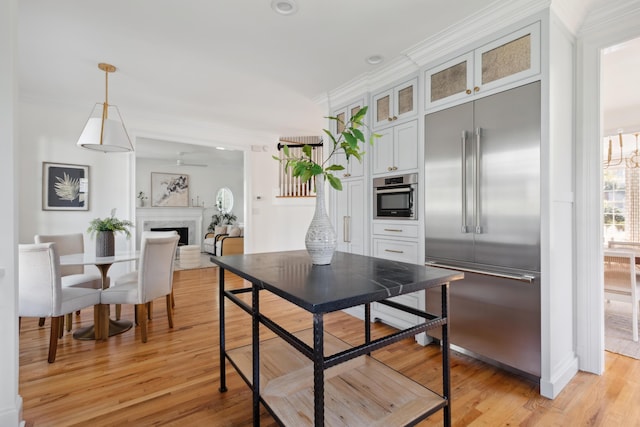 kitchen with a fireplace, light wood-style floors, appliances with stainless steel finishes, and ornamental molding