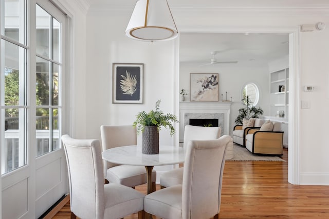 dining space with light wood finished floors, built in shelves, crown molding, ceiling fan, and a fireplace