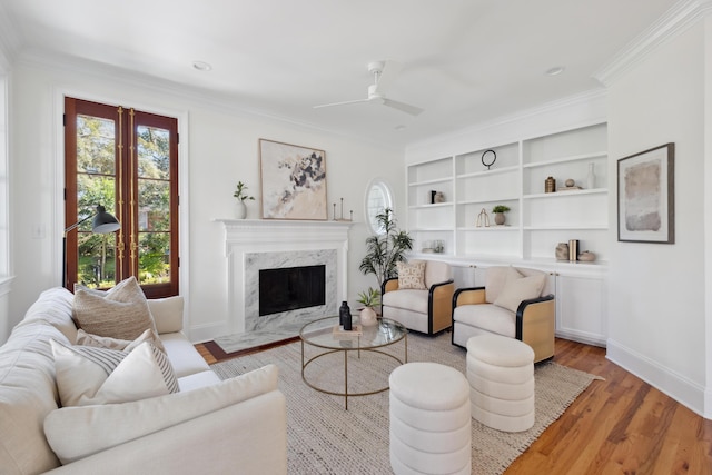 living room featuring a ceiling fan, baseboards, a premium fireplace, crown molding, and light wood-type flooring