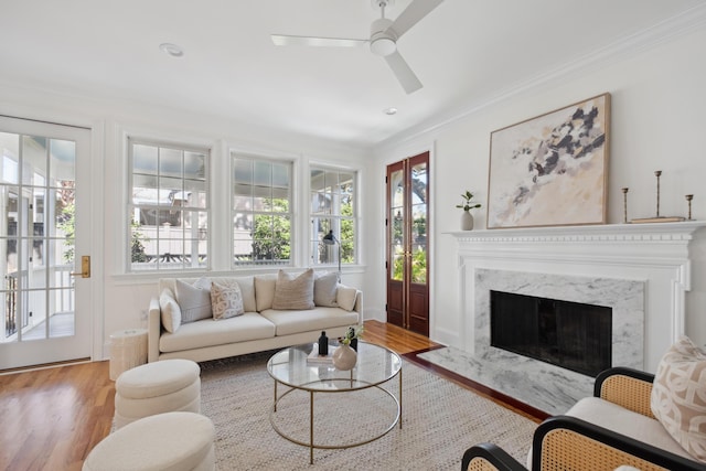 living room with ceiling fan, a premium fireplace, wood finished floors, and ornamental molding