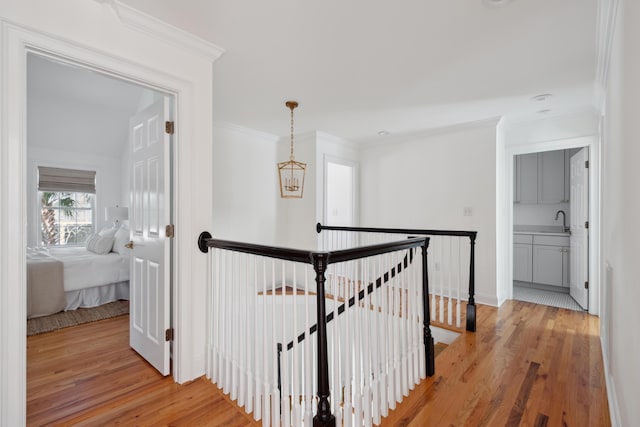 corridor featuring an upstairs landing, light wood-style flooring, crown molding, and a sink