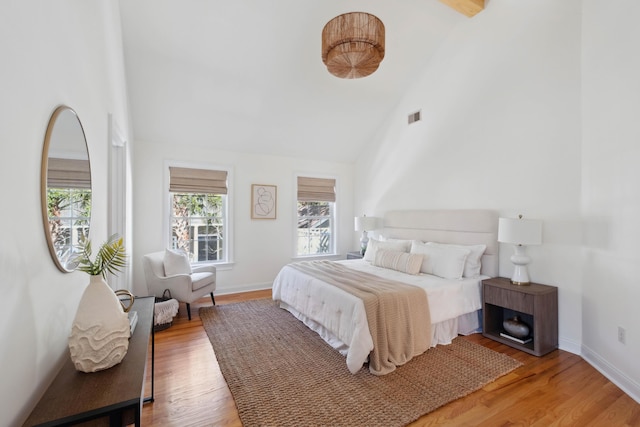 bedroom with visible vents, baseboards, high vaulted ceiling, and wood finished floors