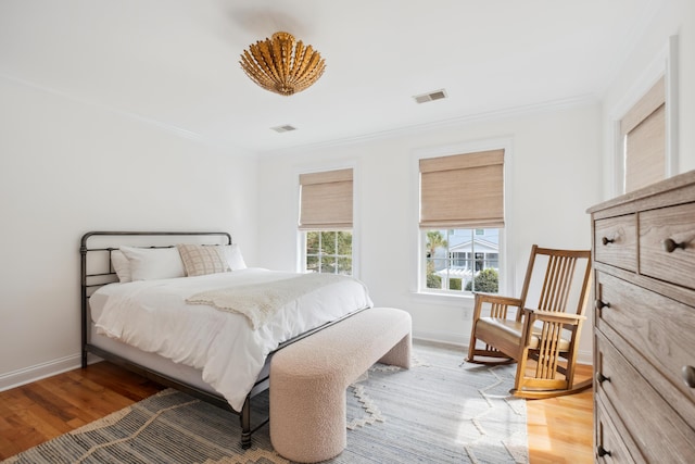 bedroom with light wood finished floors, visible vents, and ornamental molding