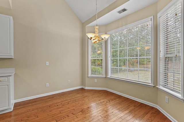 unfurnished dining area featuring lofted ceiling, a notable chandelier, visible vents, baseboards, and light wood-style floors