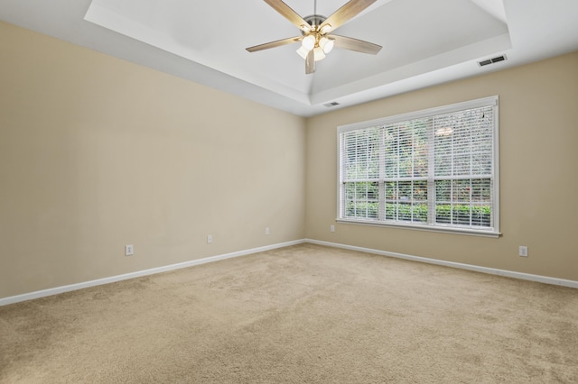 empty room with visible vents, baseboards, a raised ceiling, a ceiling fan, and light colored carpet