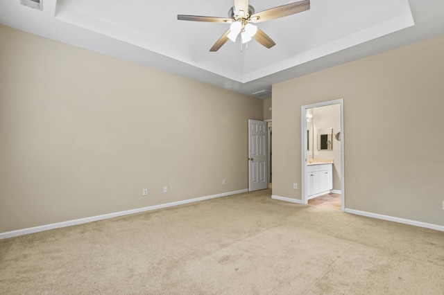 unfurnished bedroom featuring a raised ceiling, light colored carpet, a ceiling fan, connected bathroom, and baseboards