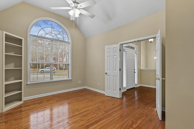 empty room with lofted ceiling, wood finished floors, a ceiling fan, and baseboards