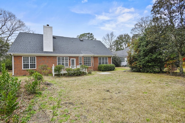 rear view of property featuring a yard, roof with shingles, a chimney, and brick siding