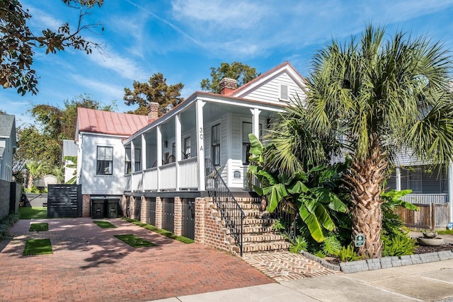 view of front of home with a chimney, covered porch, a standing seam roof, metal roof, and stairway