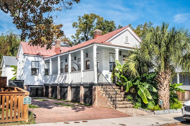 view of front of home featuring covered porch, stairway, a chimney, and metal roof