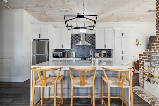 kitchen featuring wall chimney exhaust hood, appliances with stainless steel finishes, a sink, a chandelier, and dark wood-style flooring