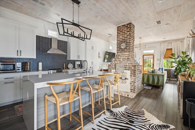 kitchen with wall chimney exhaust hood, a sink, stainless steel microwave, decorative backsplash, and white cabinets